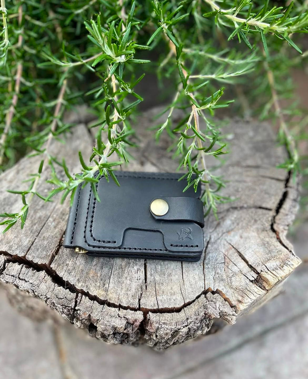 Black leather wallet on a natural wood stump with rosemary plants - lifestyle shot