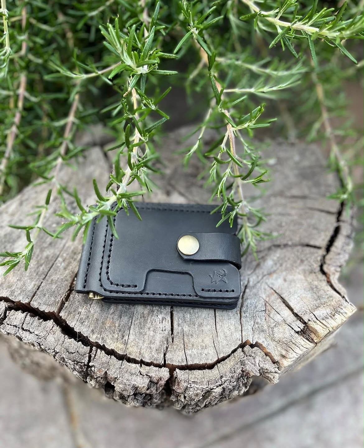 Black leather wallet on a natural wood stump with rosemary plants - lifestyle shot